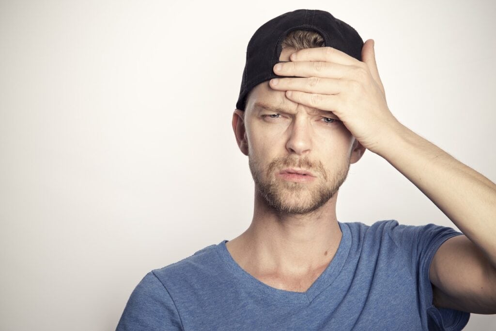 man in hat and tshirt with hand on forehead confused