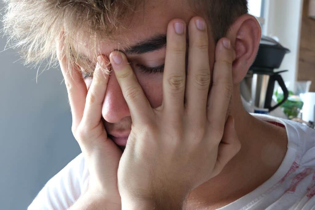 teen guy covering face with hands depressed