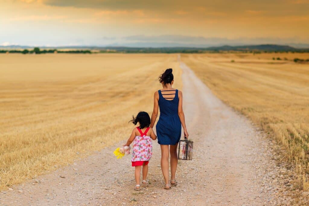 Back of mom and daughter walking desert beach holding hands