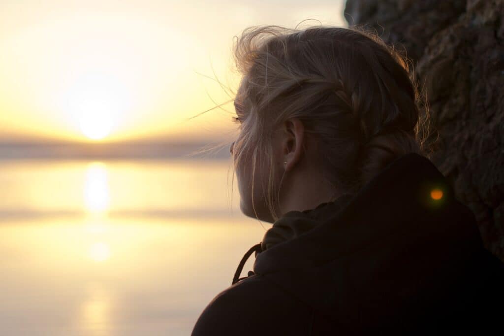 sad teen girl watching sunset over water