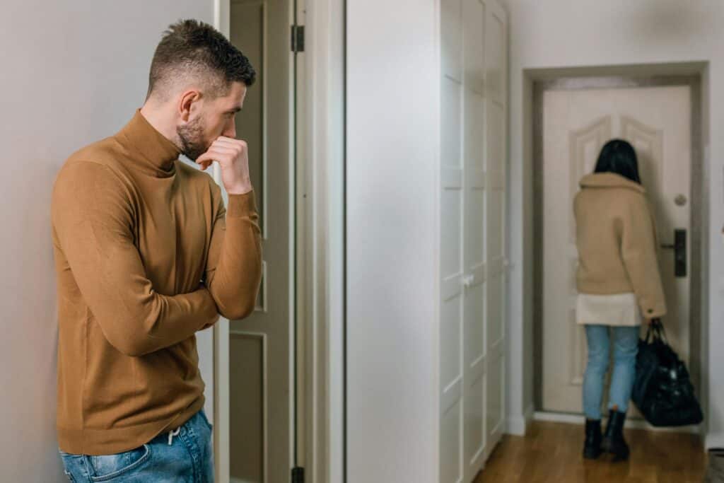 man watching as woman leaves with suitcase