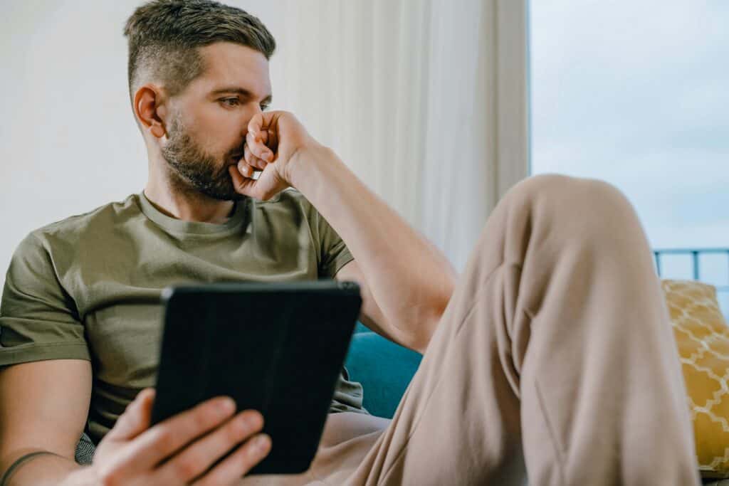 man upset sitting on couch with computer tablet