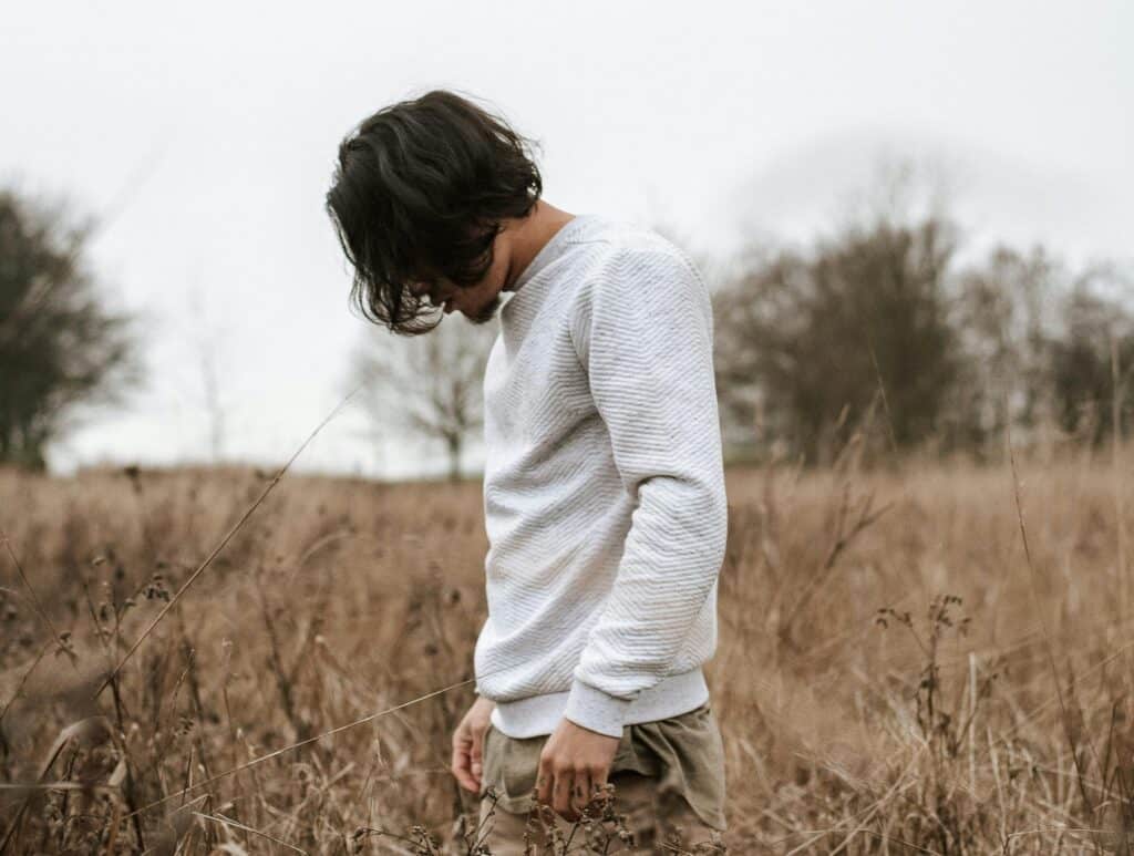 teen guy hair over face walking in field sad