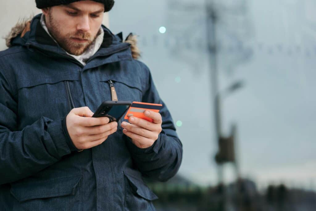 man in coat outside looking at phone and credit card