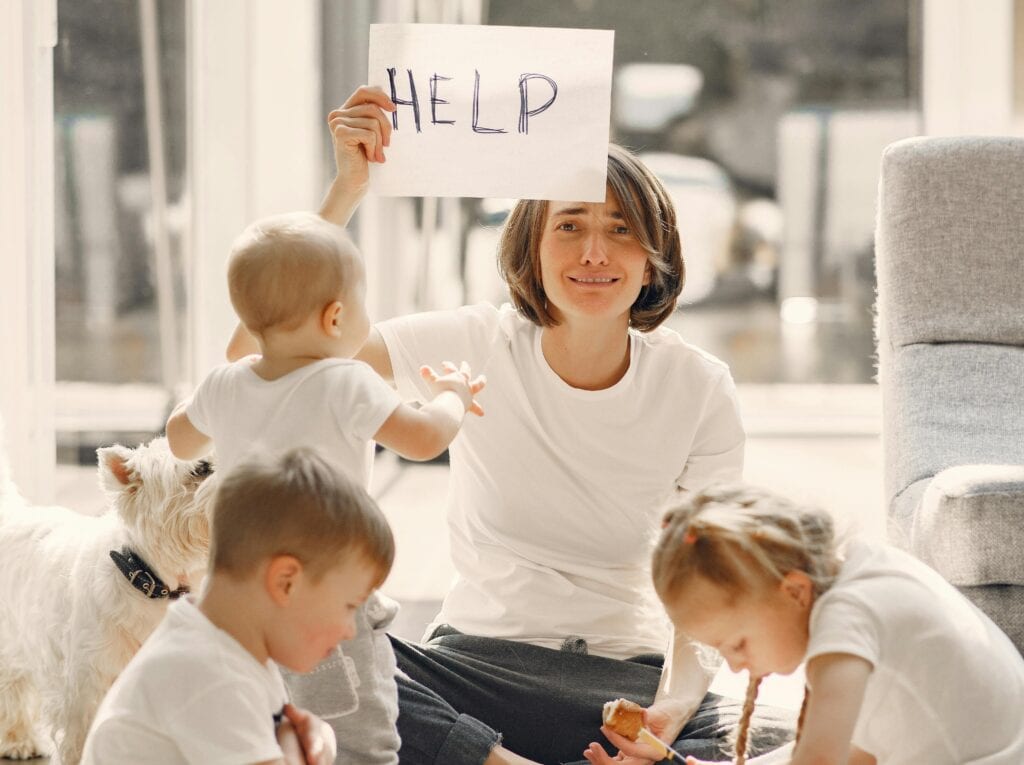 Woman surrounded by three young kids holding sign that says help