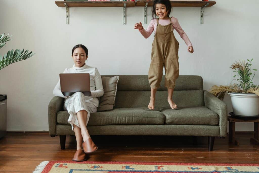 mom working on couch while daughter jumps on it