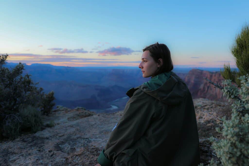 woman in coat looking out over mountain sunset