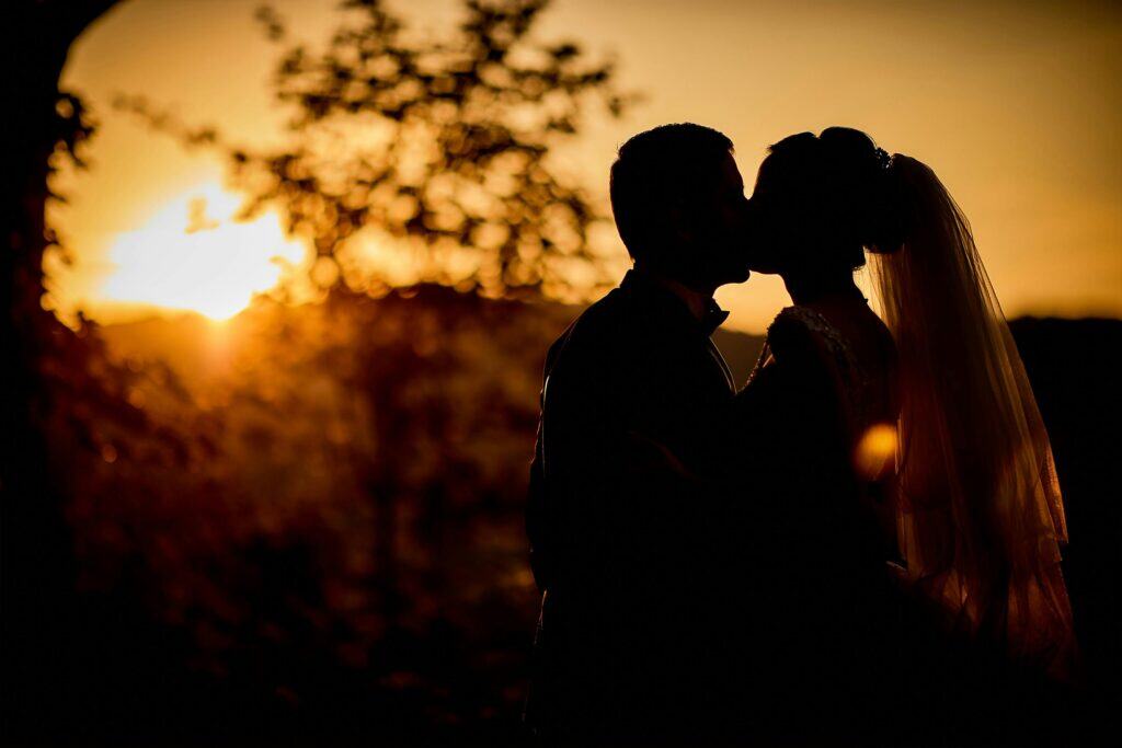 Bride and groom in shadow kissing sunset