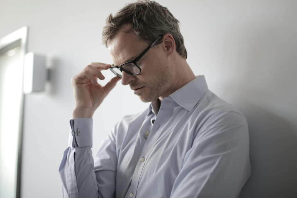 Man head bowed holding glasses upset