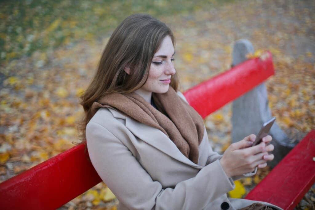 woman sitting on park bench looking at phone