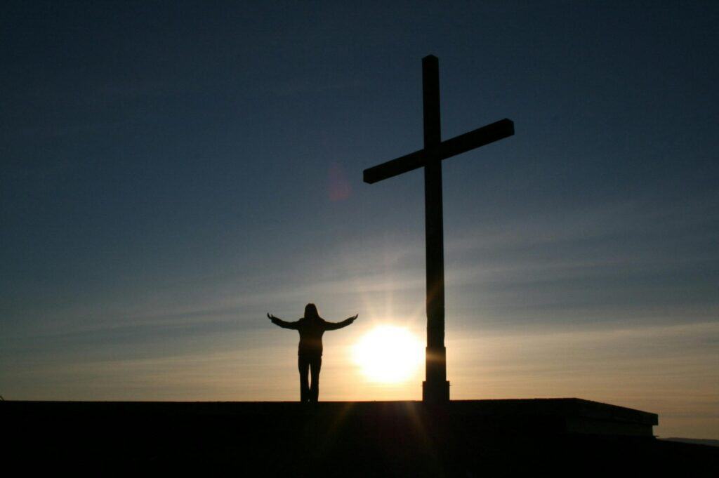 person beside large cross sunrise