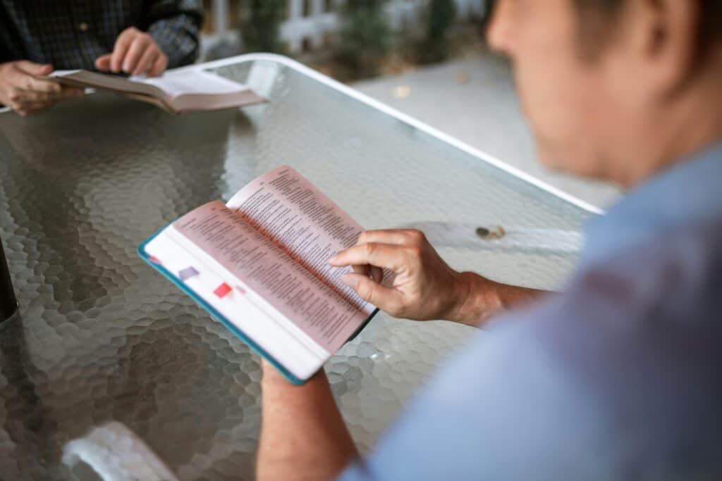 men sitting across table looking at books Bibles