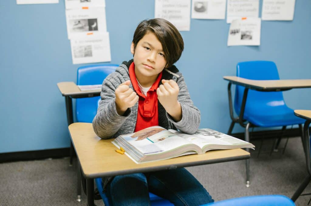 boy sitting in school desk chair holding up fists angry