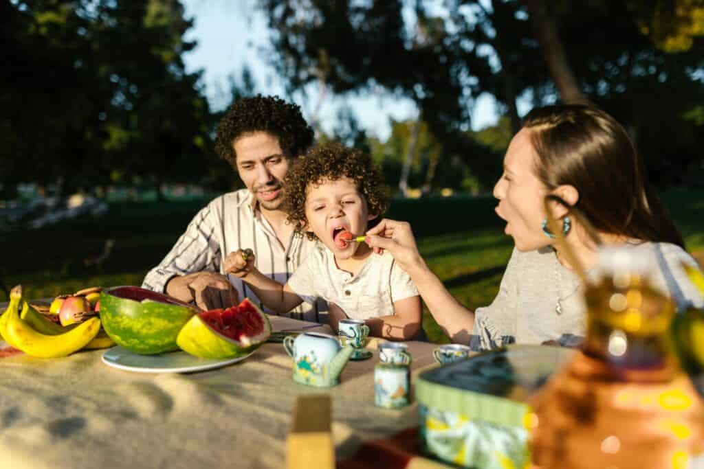 boy eating outside between parents eating fruits and veggies