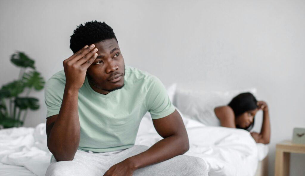 man sitting on bed woman in bed upset
