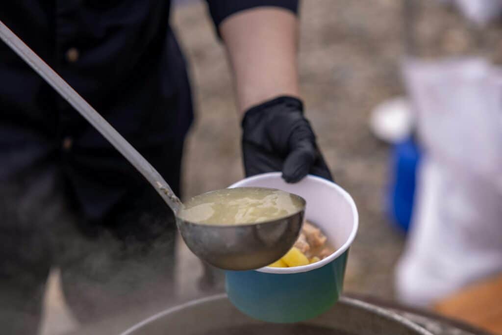 hands with gloves scooping out bowl of soup