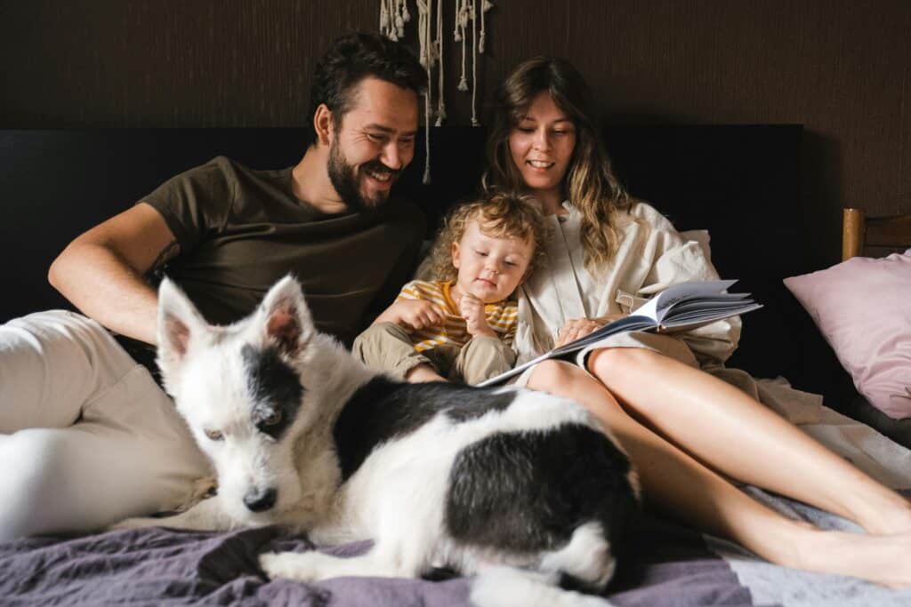 mom dad and child reading on bed with dog