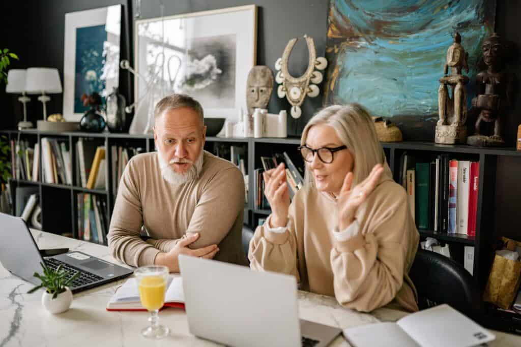 older couple retired sitting together at computers talking
