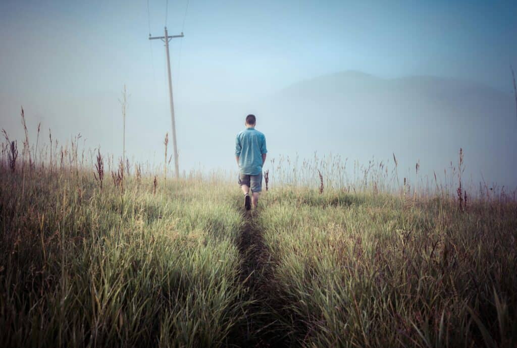 man walking away through field