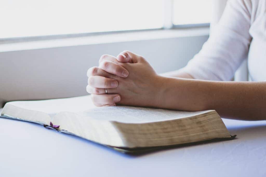 Woman's hands folded in prayer over Bible
