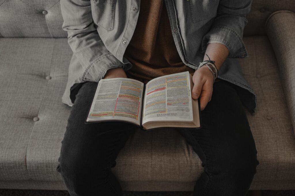 A man sits on a couch reading the Bible