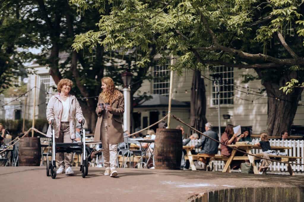 Younger woman with coffee walking with older woman with walker