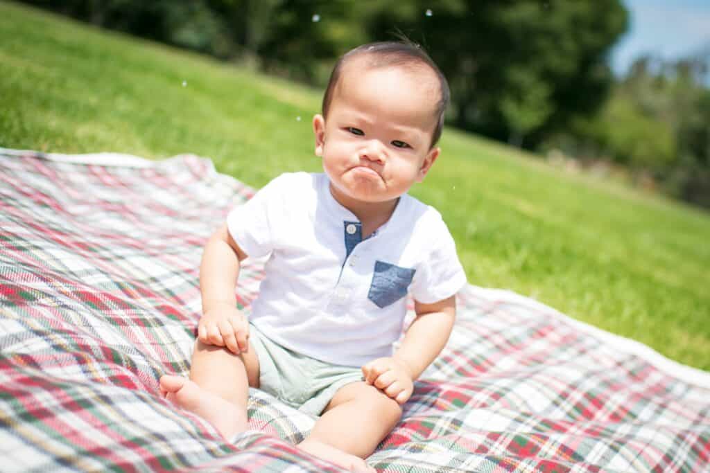 cranky toddler boy sitting on blanket
