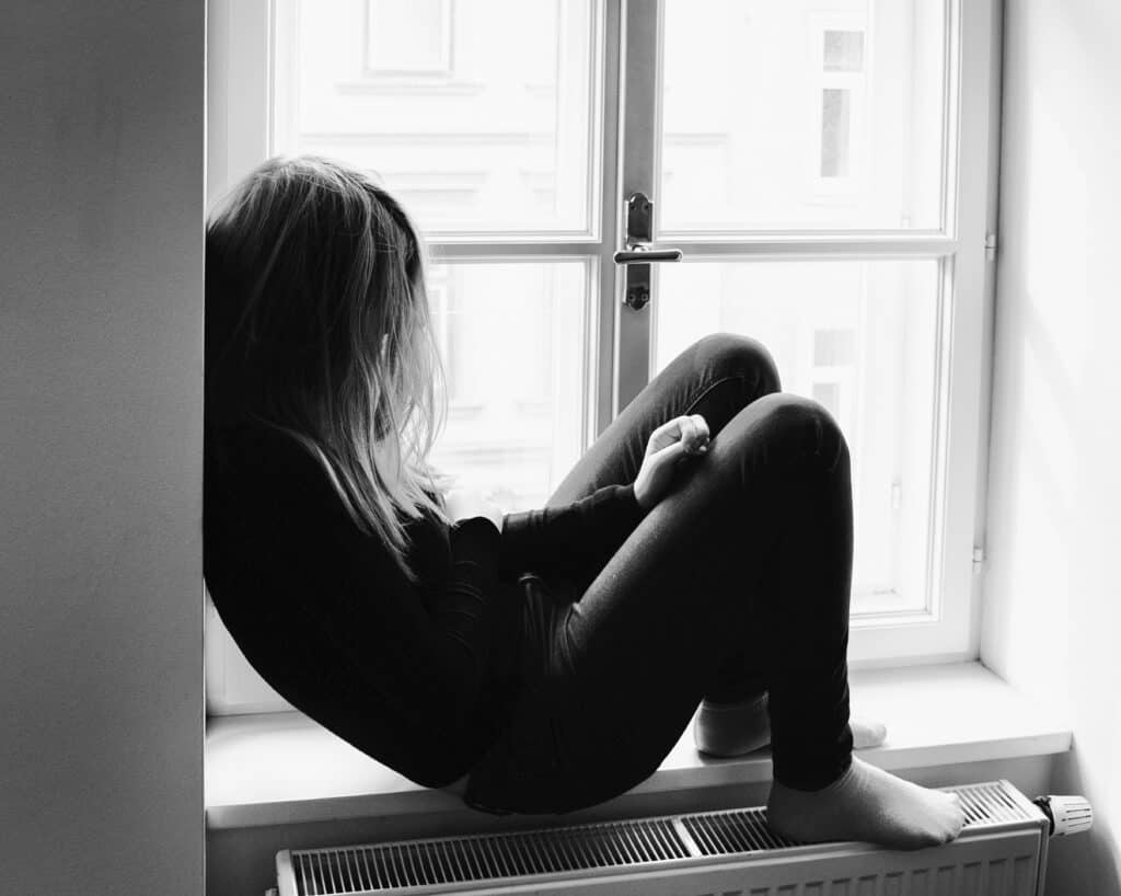 black and white silhouette of teen girl sitting on a window sill