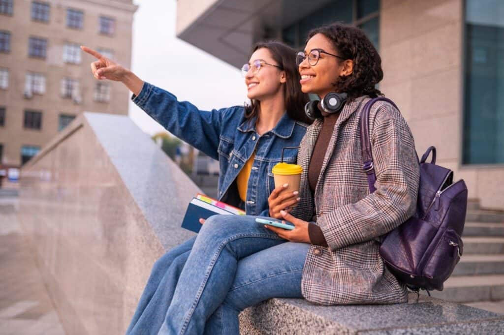 two female college students sitting on edge of building