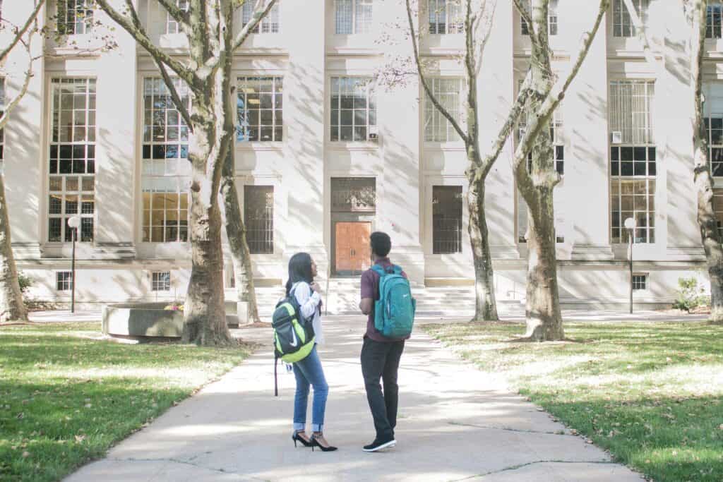 couple standing in front of college wearing backpacks