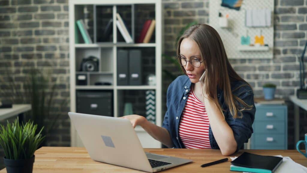 woman on phone and computer looking surprised