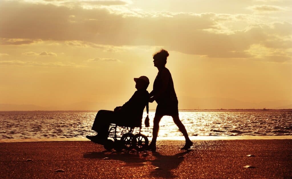 silhouettes against sunset of woman pushing man in wheelchair