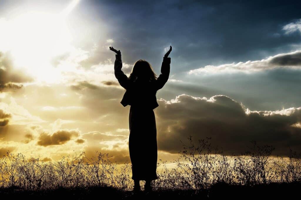 woman standing hands raised to bright sky