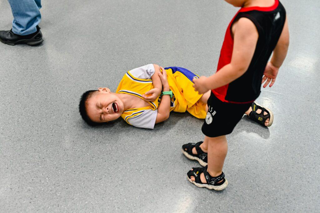 child on floor crying other child stands over him