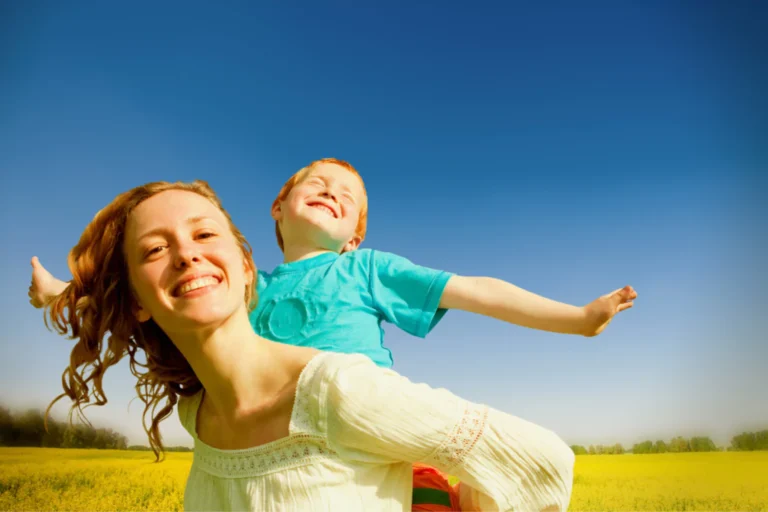Smiling single mom carrying happy child in a field, showing grit and joy in parenting.