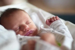 Close-up of a newborn baby sleeping peacefully in soft white clothing.