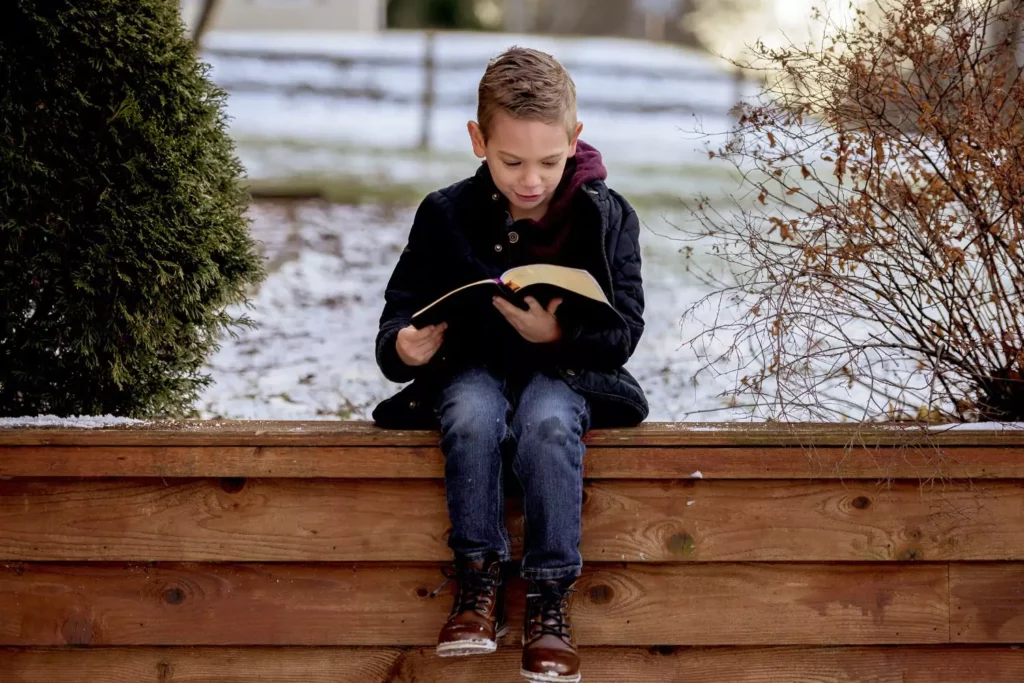 boy sitting on the wall reading his Bible in school