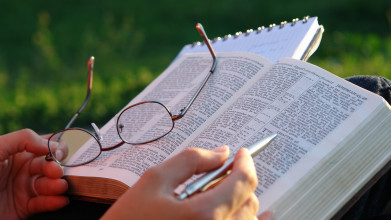 Close-up of a woman's hands holding her glasses and studying the Bible