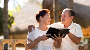 Middle-aged couple sits on an outside bench smiling and reading the Bible