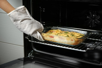 Hand in an oven mitt taking a casserole out of the oven