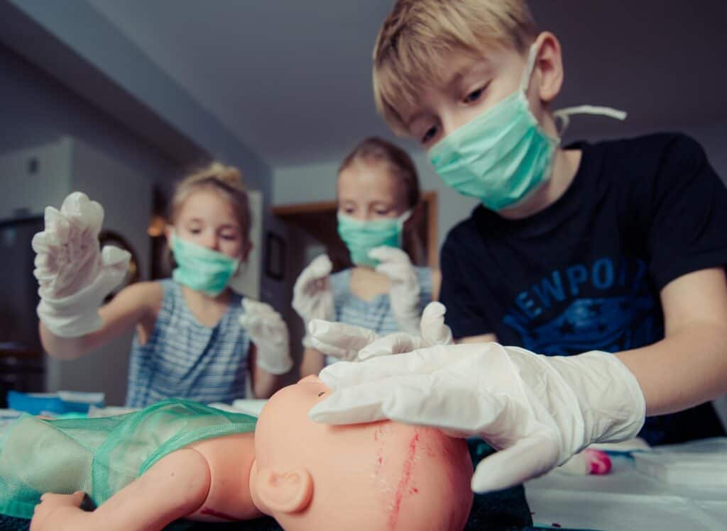 girls and boy playing doctor wearing masks and gloves with doll as patient