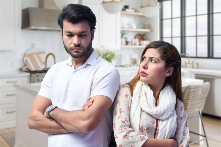 A woman looks anxiously at a man with crossed arms and a stern expression, symbolizing the tension and disconnection that happens when you don't know your spouse's apology language and your apology falls flat.