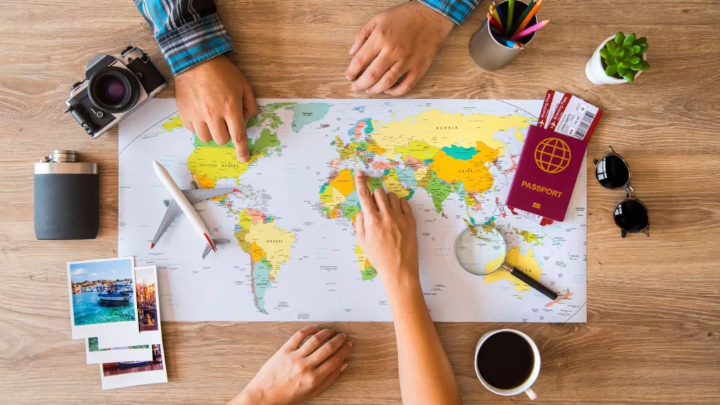 photo of a map, various travel props, and the hands of a couple pointing at the map and planning their vacation