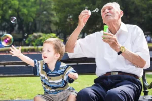 Help Your Parents and Kids Build a Strong Bond by playing together. Grandpa is blowing bubbles on a park bench while grandson is chasing them.