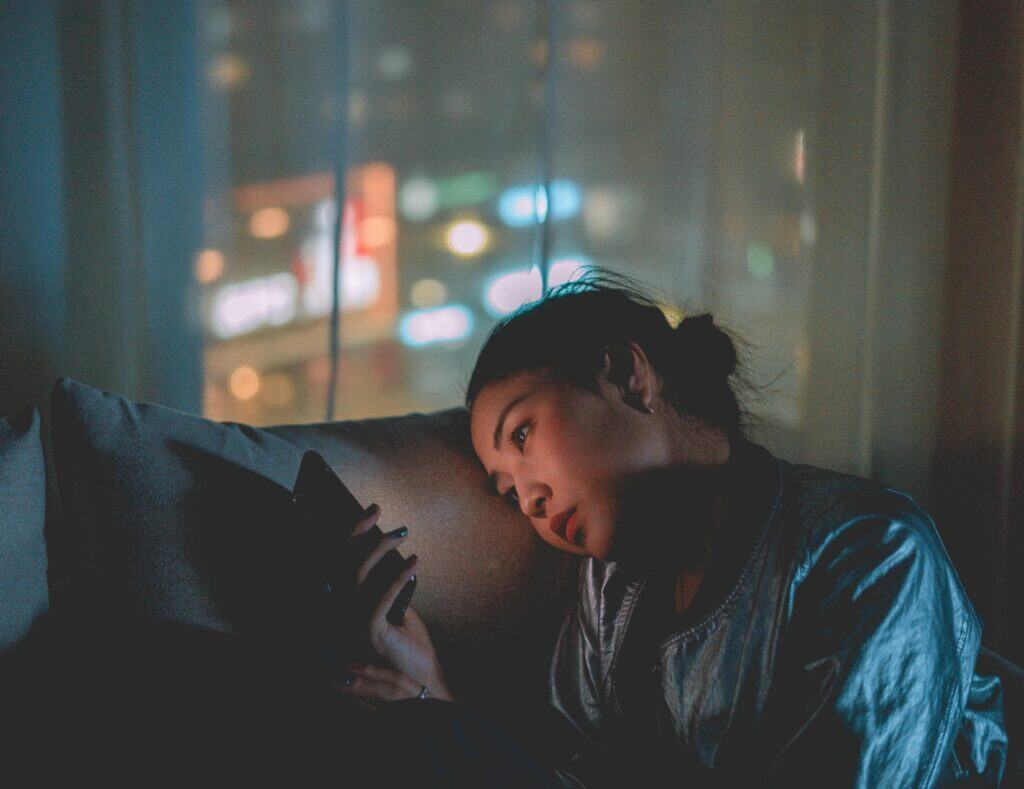 woman sitting in dark on phone looking out window