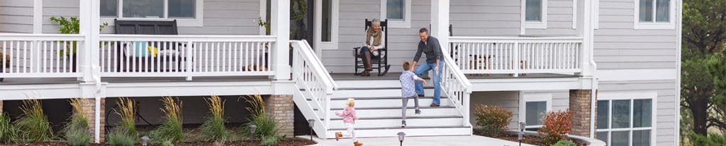 A young boy and girl run up the porch steps towards their father's open arms while their grandmother watches, smiling