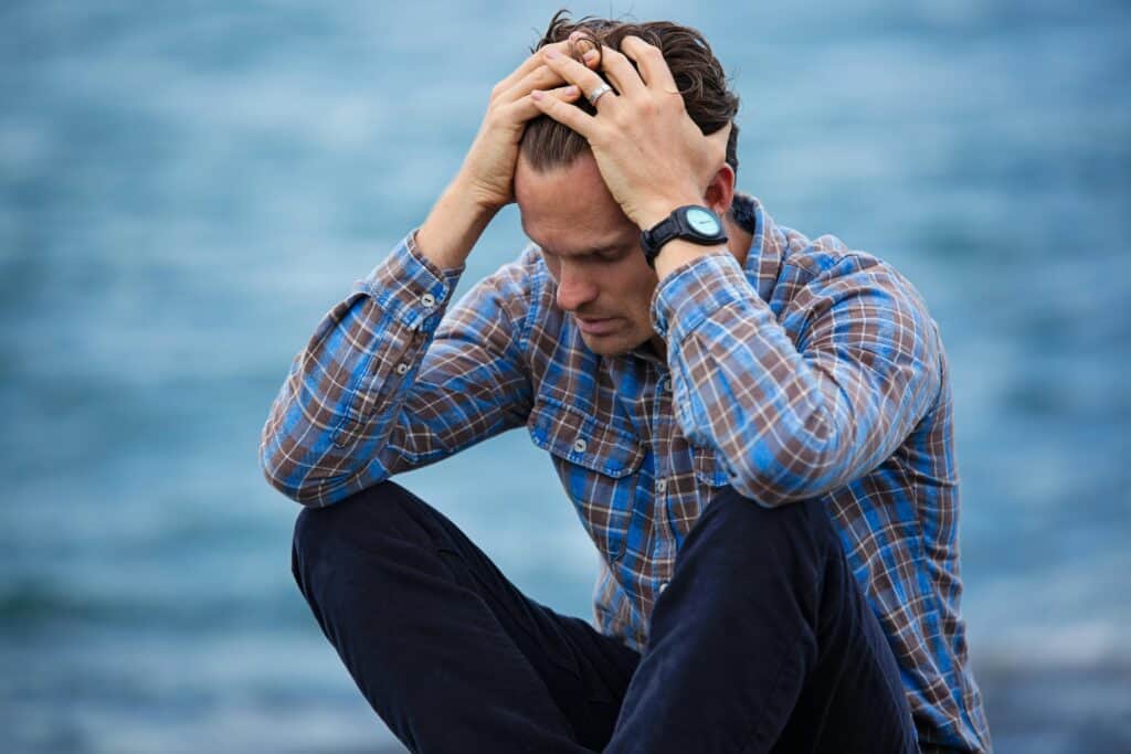 man by water holding his head looking depressed