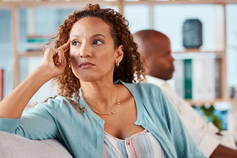 Frustrated woman sitting on couch, reflecting on emotional distance and financial infidelity in marriage.
