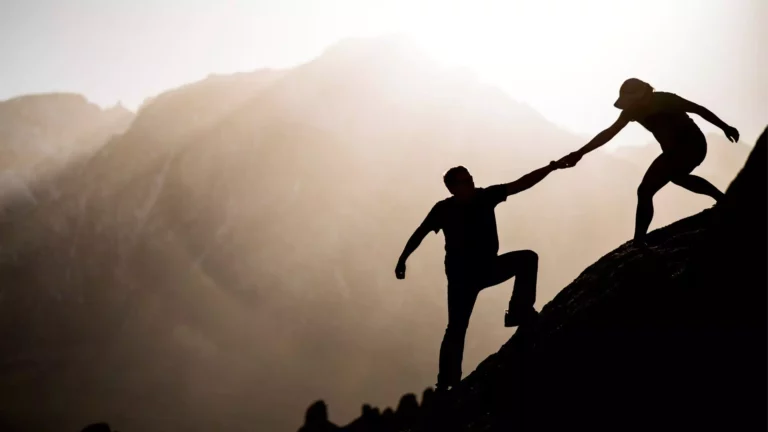 silhouette of woman helping a man up a mountain. This is symbolic of hope in marriage through mental illness.