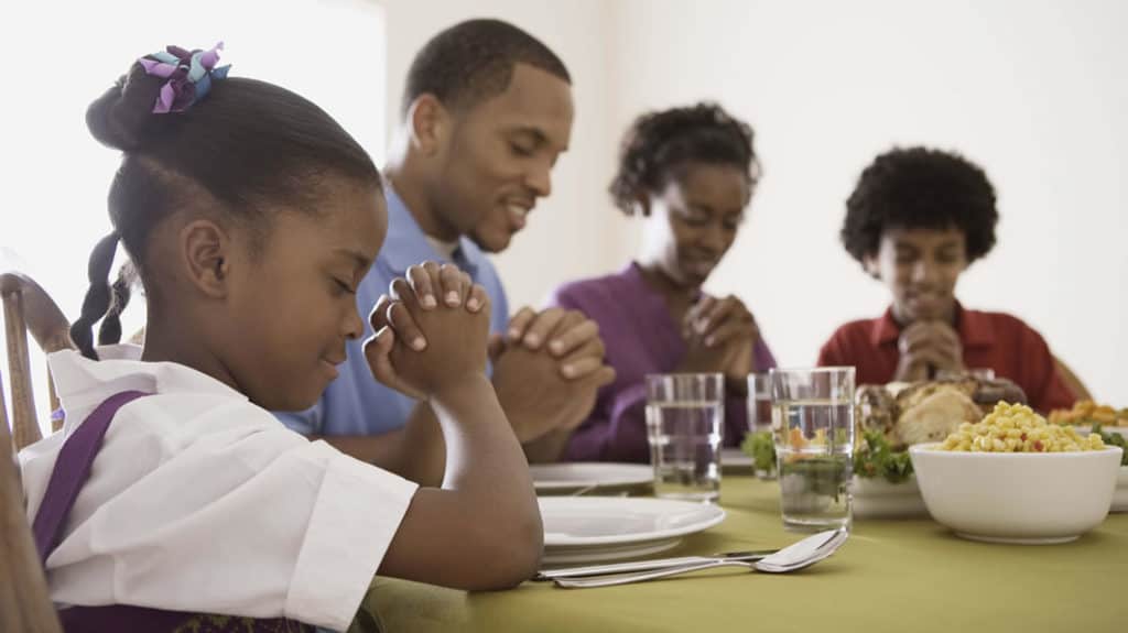 Smiling African-American family seated at the dinner table, saying grace